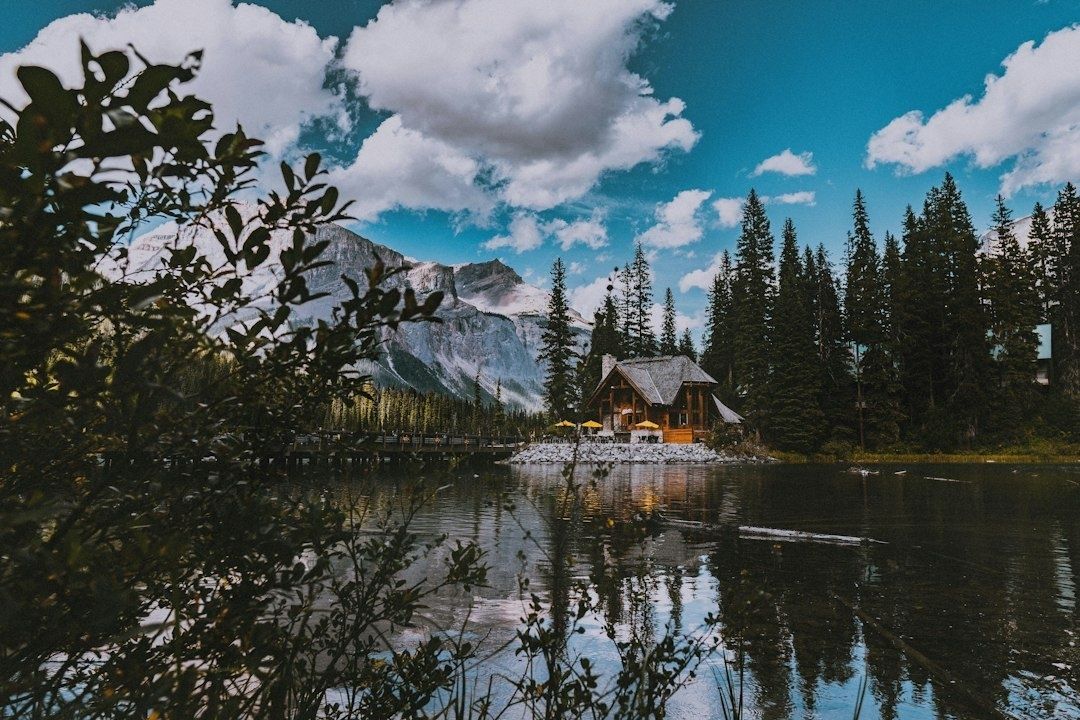 Tømmerhytte ved en innsjø med fjell og barskog i bakgrunnen